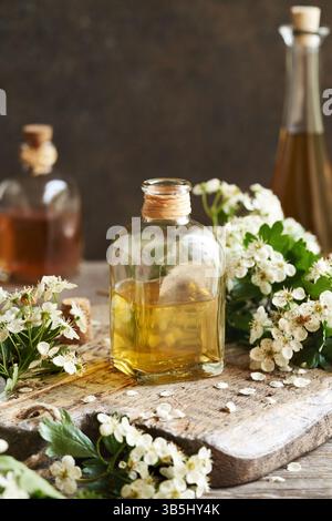 Une bouteille de teinture à base de plantes avec des fleurs d'aubépine fraîches sur une table au printemps Banque D'Images