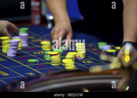 Table de roulette avec des mains humaines déposant des jetons dans le casino. Roue de roulette au premier plan. Jeu de pari. Des gens méconnaissables Banque D'Images