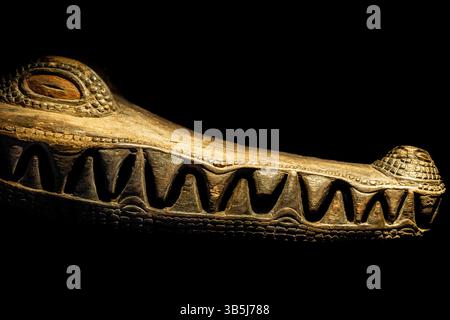 Gros plan d'un visage de crocodile en bois méticuleusement sculpté, mettant en valeur un savoir-faire artisanal détaillé sur fond sombre et sombre. Banque D'Images