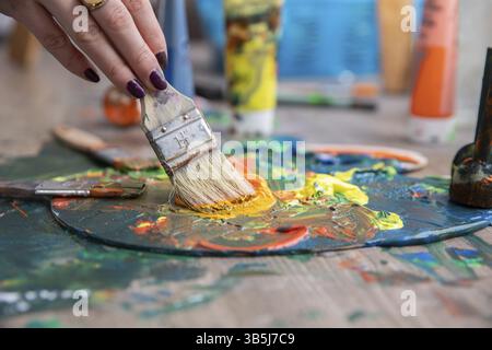 Un gros plan détaillé d'une main mélangeant habilement des peintures vibrantes et colorées sur une palette avec des pinceaux Banque D'Images