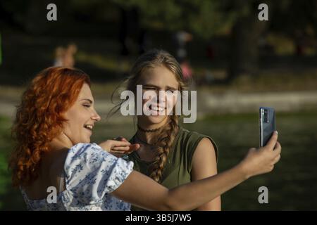 Par une journée ensoleillée, deux amis proches apprécient la compagnie, riant et prenant un selfie amusant à l'extérieur Banque D'Images