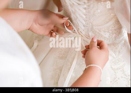 Mariée se préparer : une demoiselle d'honneur attache le corset d'une belle robe de mariée. Banque D'Images