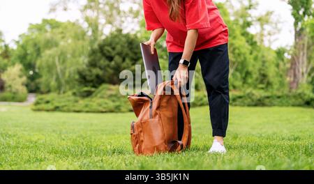 Femme urbaine prenant l'ordinateur portable hors du sac à dos dans le parc de la ville Banque D'Images