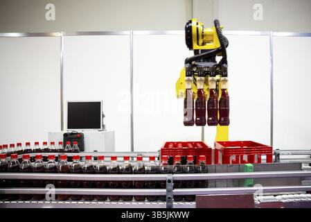Le bras robotique jaune dispose les bouteilles de soda en plastique dans une caisse ð emballage. EQUIPEMENT de machines industrielles automatiques Banque D'Images