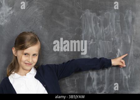 Une écolière se montre sur un conseil scolaire vide. Il est debout dans la salle de classe au tableau. Jeune fille Banque D'Images