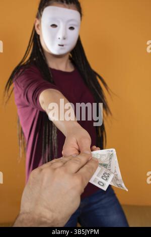 La main masculine prend de l'argent à un étranger qui a un masque partout sur son visage afin que personne ne le reconnaisse. De l'argent promis dans un prêt anonyme Banque D'Images