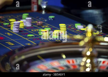 Table de roulette avec des mains humaines déposant des jetons dans le casino. Roue de roulette au premier plan. Jeu de pari. Des gens méconnaissables Banque D'Images