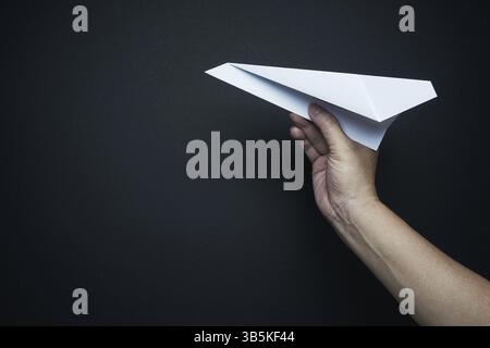 Main tenant l'avion de papier sur fond noir, concept de plan de voyage Banque D'Images