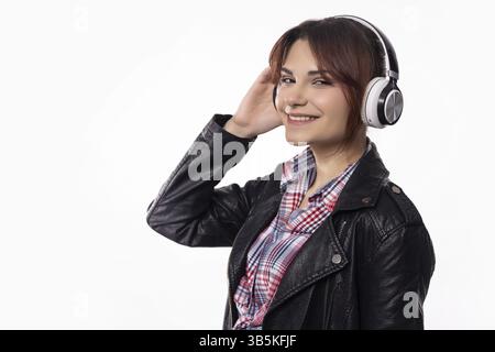 Une jeune femme joyeuse dans des écouteurs élégants profite de sa musique préférée, habillée dans une tenue tendance mettant en valeur son style Banque D'Images