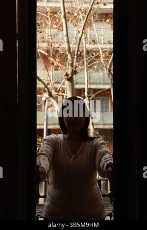 Une femme se tient devant une fenêtre, les bras tendus. L'image a une humeur de solitude et d'isolement, car la femme est seule Banque D'Images