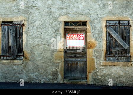 Une maison rustique en pierre présente une façade altérée et des fenêtres avec armatures. Un panneau rouge vif annonce que la propriété est à vendre. France Banque D'Images