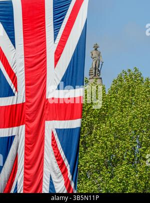 Londres, Royaume-Uni. La statue Nelson au sommet de la colonne Nelson à Trafalgar Square, vue de Whitehall, derrière un arbre et un drapeau de l'Union suspendu à l'extérieur Banque D'Images