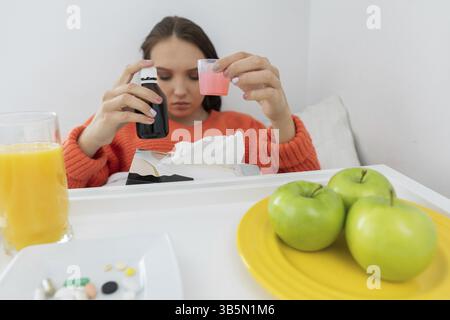 Le médicament dans une petite tasse. Il est assis sur son lit. Un adolescent malade. Un froid profond Banque D'Images