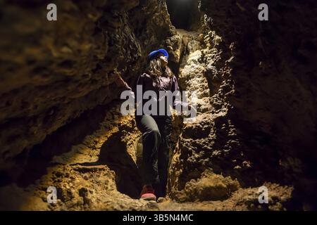 Young tourist woman explores the inside of a beautiful colourful cave. Flowstones, stalactites and stalagmites lighted in different vivid colours. Ven Banque D'Images