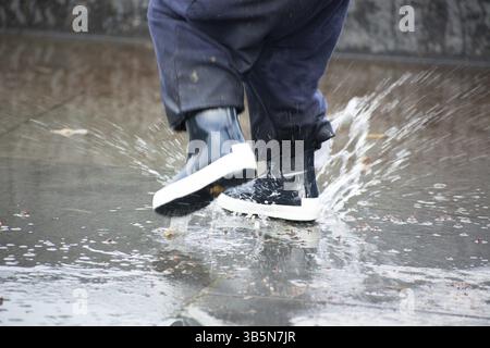 Close-up of kid bleu portant des bottes de pluie et de marcher pendant le grésil, pluie et neige sur journée froide. Dans l'enfant des vêtements de mode colorée de sauter dans un complexe immobilier Banque D'Images