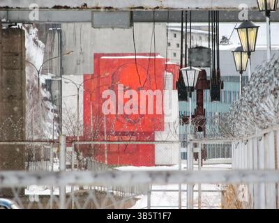 Krasnoïarsk, Russie - 10 février 2019 : Portrait de Lénine sur un ancien bâtiment soviétique visible de derrière une clôture de barbelés. Banque D'Images