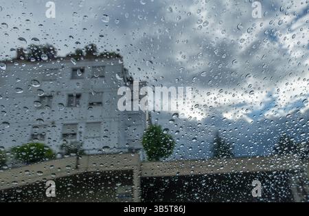 Vue des jours de pluie par une fenêtre, mettant en évidence les gouttelettes et un bâtiment flou. Banque D'Images
