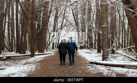 Couple mûr allant sur le chemin enneigé à la forêt de pins d'hiver. Mari senior et femme marchant à travers le sentier dans la forêt de conifères. Ancienne paire de Banque D'Images