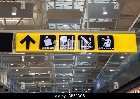 Fiumicino, ROM, Italien - 24 avril 2025 : un panneau jaune vif dans un terminal d'aéroport affiche des icônes pour le shopping, les restaurants, un espace fumeur, un Banque D'Images