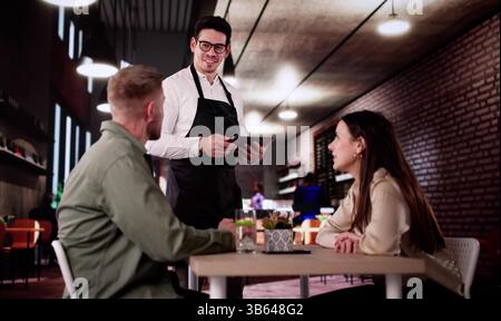 Le serveur romantique prend le menu du dîner commande de Happy Elegant couple. Banque D'Images