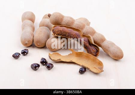 Fruits de tamarin, entiers, cassés ouverts, et graines sur une planche de bois clair. Fruits bruns en forme de gousses de Tamarindus indica, au goût aigre-doux. Banque D'Images