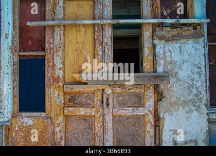 Gros plan d'une porte en bois qui s'effondrait et arborait avec de la peinture fissurée et écaillée dans les tons de jaune, bleu et brun. Banque D'Images