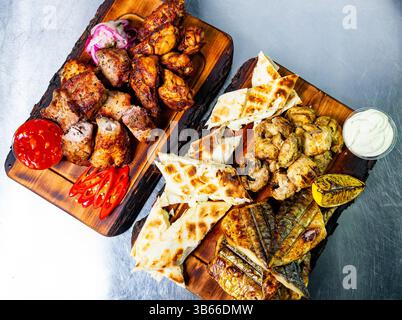 Un délicieux assortiment de poulet grillé, de poisson et de plats savoureux disposés sur des plateaux en bois. Les légumes frais et les sauces ajoutent une touche vibrante à Banque D'Images