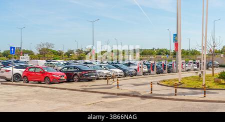 Loule, Portugal- 27 avril 2025. Rangée de voitures garées à côté des Superchargeurs Tesla dans un terrain pavé. Banque D'Images
