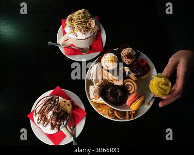 Une vue descendante d'une table avec deux tasses de café surmontées de crème fouettée et de filet de chocolat, et un stand à deux niveaux rempli d'une variété de sm Banque D'Images