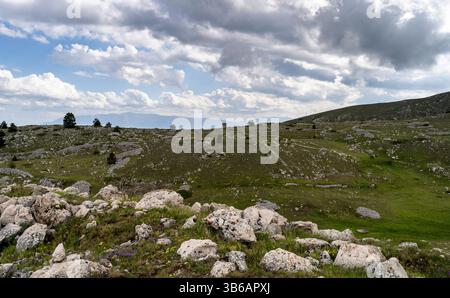 Un paysage pittoresque avec des collines vallonnées, un terrain rocheux et un ciel nuageux. Le premier plan est parsemé de grosses pierres et de taches d'herbe verte, wh Banque D'Images