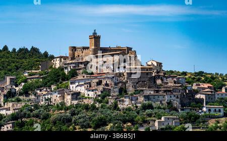 Un pittoresque village perché avec un château médiéval et des maisons en pierre entourées d'une végétation luxuriante et d'un ciel bleu. Banque D'Images