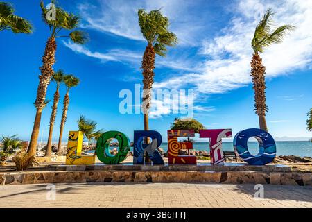 Loreto, basse-Californie du Sud, Mexique. 10 décembre 2024. Lettres colorées du nom de la ville sur la promenade touristique, les palmiers, la baie et la mer de ​​Cortez en BA Banque D'Images