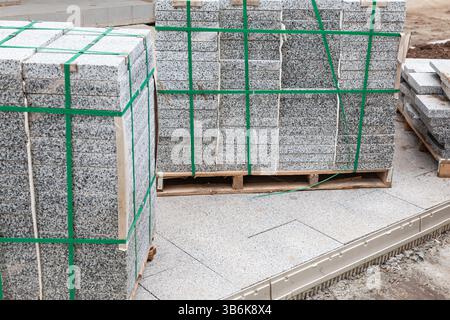 Paquets de nouvelles tuiles de granit de pavage empilées sur des palettes pour la pose sur la route. Banque D'Images