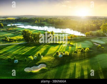 Vue aérienne du coucher de soleil sur le parcours de golf avec des arbres et des lacs aux couleurs printanières Banque D'Images