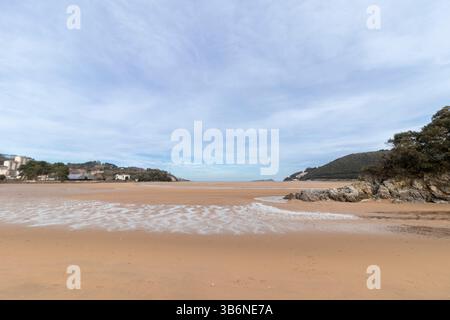 De douces vagues se répandent sur le sable doré à marée basse, révélant des rochers et créant un paysage côtier serein Banque D'Images