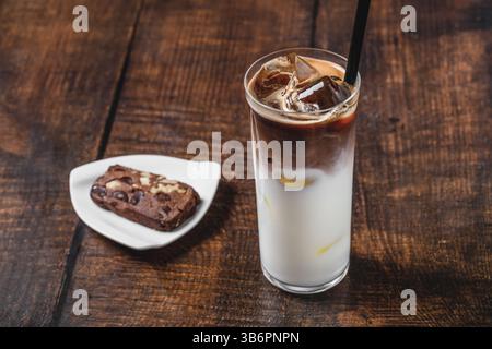 Grand verre rempli de glace, avec du café glacé mélangé à de la crème sur une table en bois Banque D'Images