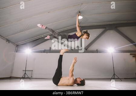 Le thème de l'Acroyoga et postures de yoga. Acroyogis. pratique avec rétro-éclairage studio. l'homme de base lance la femme Pop Flyer en vol jusqu'. Acr Position Banque D'Images