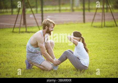 Asseyez-vous fitness couple s'entraîner asseyez-vous dehors dans l'herbe Fit personnes s'entraînant en cross training. Femme faisant des crunches abdominales presser l'exercice avec tr Banque D'Images