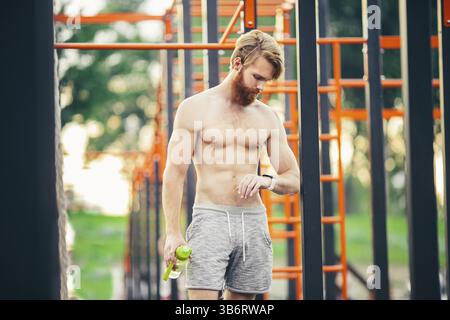 Homme de sport regardant la montre debout Treet gym. Jeune athlète musclé vérifiant les résultats sportifs sur montre intelligente après un bon entraînement. Homme après w Banque D'Images