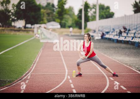 Les femmes de race blanche de condition physique faisant l'échauffement avant l'exercice. Étirement des jambes de l'athlète faisant l'échauffement avant l'entraînement. Le jogging dans la ville au Stadium Banque D'Images