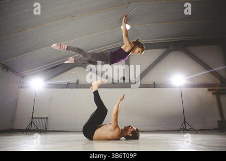 Le thème de l'Acroyoga et postures de yoga. Acroyogis. pratique avec rétro-éclairage studio. l'homme de base lance la femme Pop Flyer en vol jusqu'. Acr Position Banque D'Images
