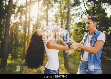 Élégant jeune famille maman, papa et fille un an blonde assis avec le père sur les épaules jouant heureux et souriant, à l'extérieur en dehors de la ville i. Banque D'Images