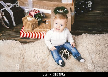 Thème hiver et vacances de Noël. Enfant garçon caucasien blond 1 an assis à la maison près de l'arbre de Noël avec décor du nouvel an sur tapis shaggy Banque D'Images