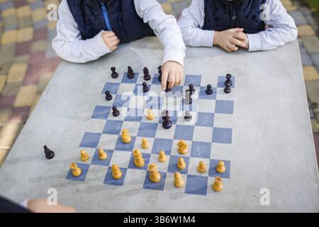 Concept d'éducation, jeu intellectuel. Tournoi d'échecs, leçon, camp, concept d'entraînement. Gros plan des mains d'enfants jouant aux échecs sur un échiquier dessiné Banque D'Images