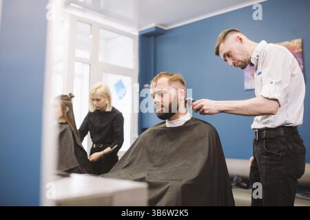 Gros plan d'un homme d'obtenir un coupe très tendance à un salon de coiffure. Portrait masculin coiffure desservant un client. Homme barbu avec une décote de t Banque D'Images