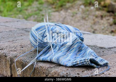fil de chaussette bleu clair dans le processus de tricotage de chaussettes, avec des aiguilles à tricoter, couché sur une surface de pierre Banque D'Images