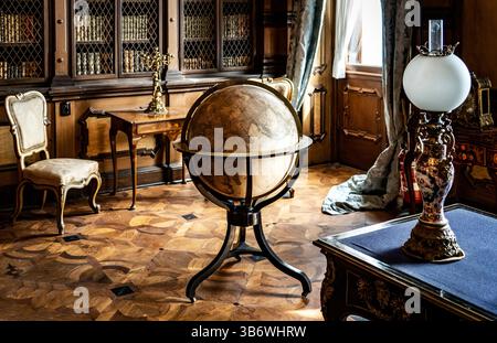 Un globe vintage sur un stand dans un cadre élégant de bibliothèque, entouré de meubles anciens et d'un éclairage chaleureux. Banque D'Images