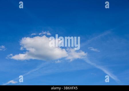De magnifiques nuages blancs dérivent à travers un ciel bleu éclatant, avec des traînées d'avion qui sillonnent l'atmosphère, créant une scène sereine Banque D'Images