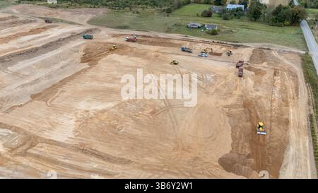 Vue aérienne d'un chantier de construction avec de la machinerie lourde, y compris des bulldozers et des camions, travaillant sur une grande surface de terrain dégagée. Le paysage est m Banque D'Images