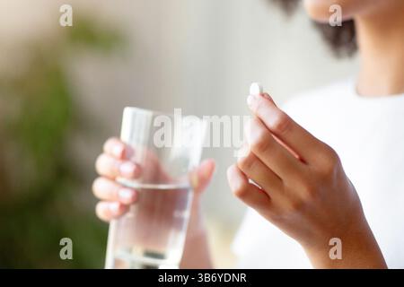 Femme souriante prenant la pilule blanche ronde, tenant le verre d'eau à la main Banque D'Images